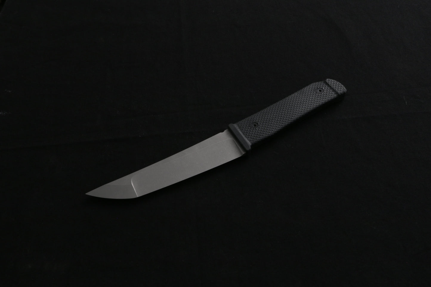 Fixed blade Kwaiback Knife, black G10 handle, stone wash blade, on a dark surface
